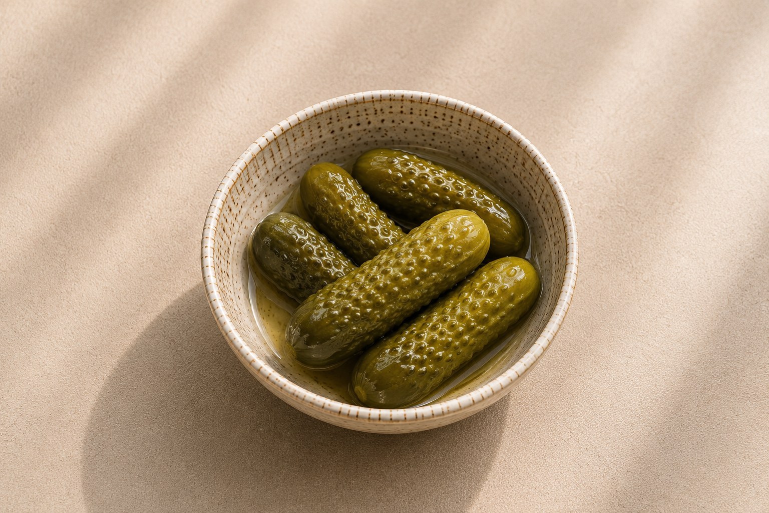 Whole glossy pickles in brine in a ceramic bowl.